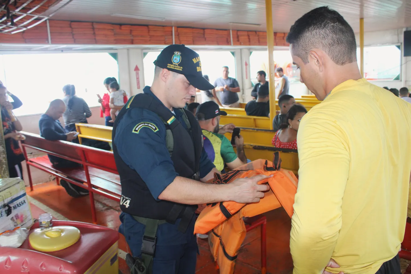 Inspetor naval da Marinha confere um colete salva-vidas com um tripulante a bordo de um barco de passageiros